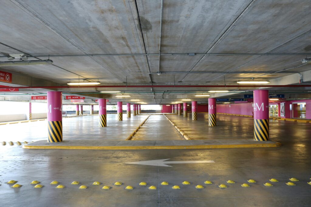 Commercial Parking Lot and Garage Cleaning Services Empty indoor parking deck with pink pillars and clear directional signs in Santo Domingo.
