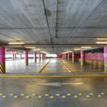 Commercial Parking Lot and Garage Cleaning Services Empty indoor parking deck with pink pillars and clear directional signs in Santo Domingo.