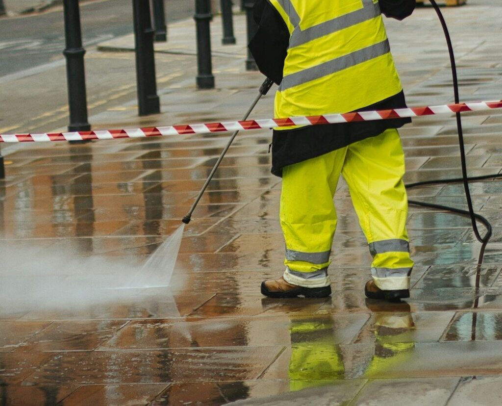 a man in a yellow jacket is using a pressure washer. Norfolk Pressure washing
